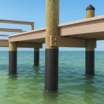 Wooden pier supported by black-coated posts over clear greenish water.
