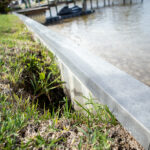 A metal retaining wall beside a grassy riverbank.