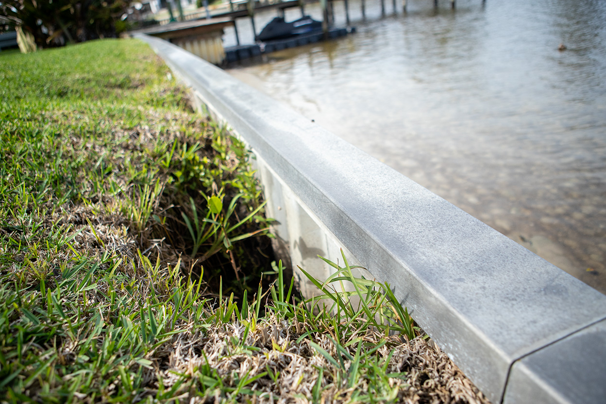 A metal retaining wall beside a grassy riverbank.