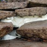 White foam or substance between uneven brown rocks.