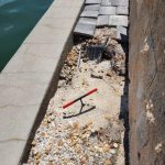 Construction tools on a gravel surface by a waterfront wall.